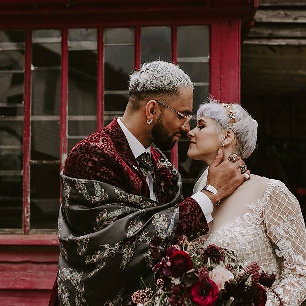 Stylish groom in red blazer and silk shawl kissing his bride