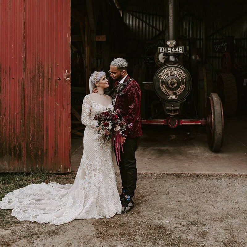 Bride in Lillian West wedding dress and groom in pink blazer next to a steam engine
