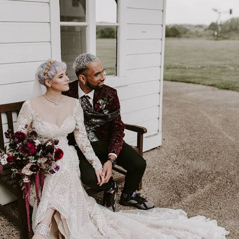 Stylish bride and groom sitting on a bench together with bride in Lillian West wedding dress