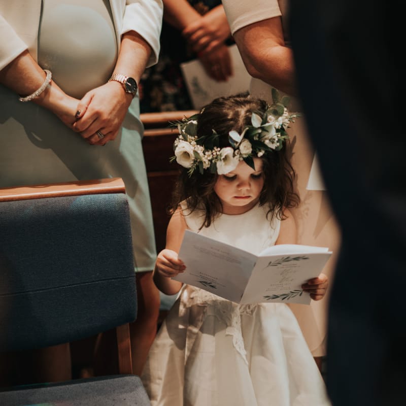 Cute flower girl in white dress and flower crown for church ceremony