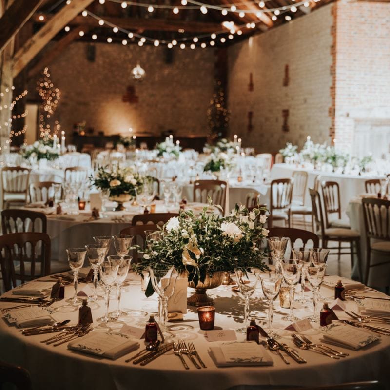 Festoon lighting drapes over wedding tables decorated in white flowers at Bury Court Barn