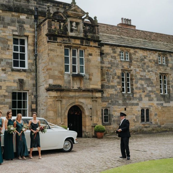 Bridesmaids wearing emerald green dresses at country house wedding ceremony with vintage car