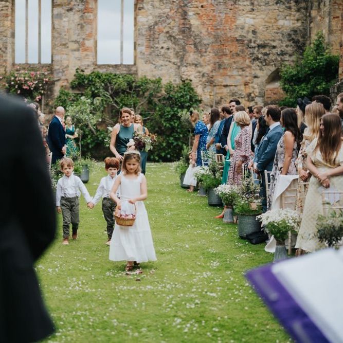 Flower girl walking down the aisle at outdoor ceremony with olive trees