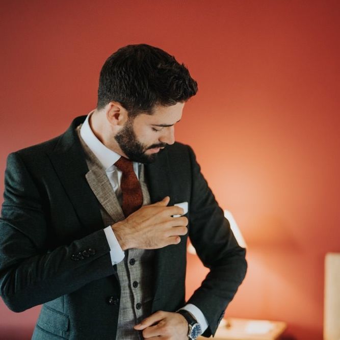 Groom getting ready wearing a three piece suit with a red tie