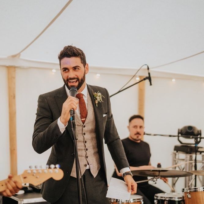 Groom wearing three piece suit and red tie at marquee reception
