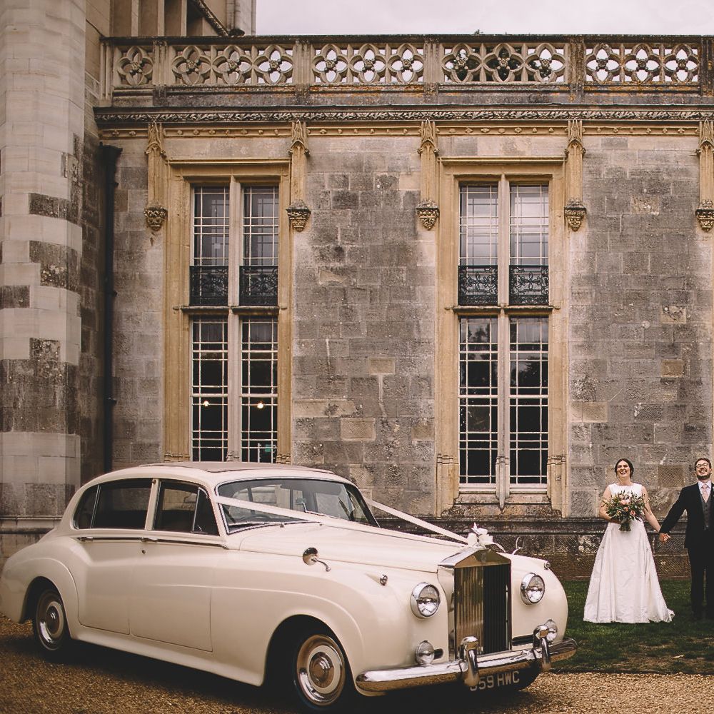 Bride and Groom Stnding in From top Their Castle Wedding Venue with Classic Wedding Car