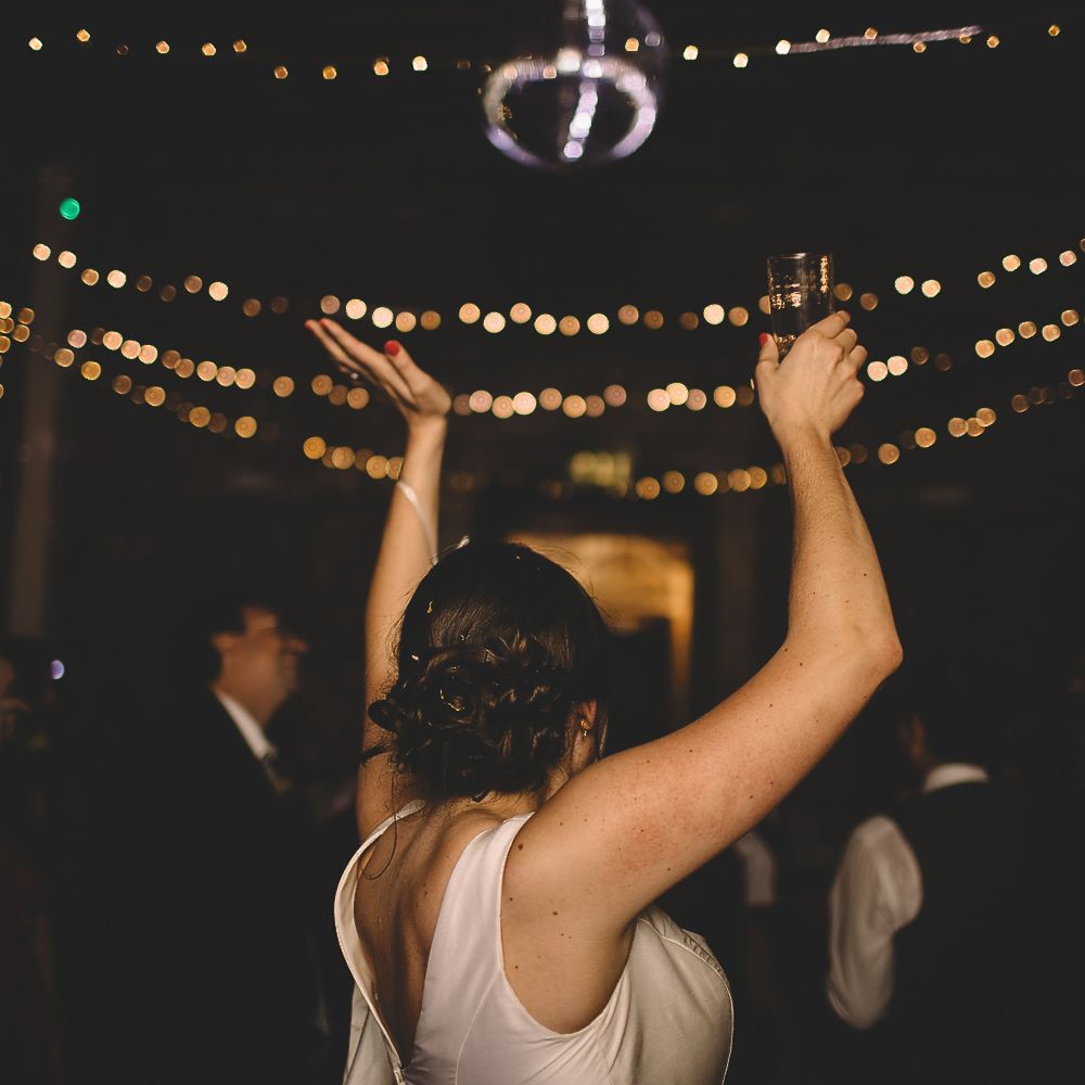 Bride in Homemade Wedding Dress with Bow Back Detail Dancing at Evening Reception with Fairylight Backdrop
