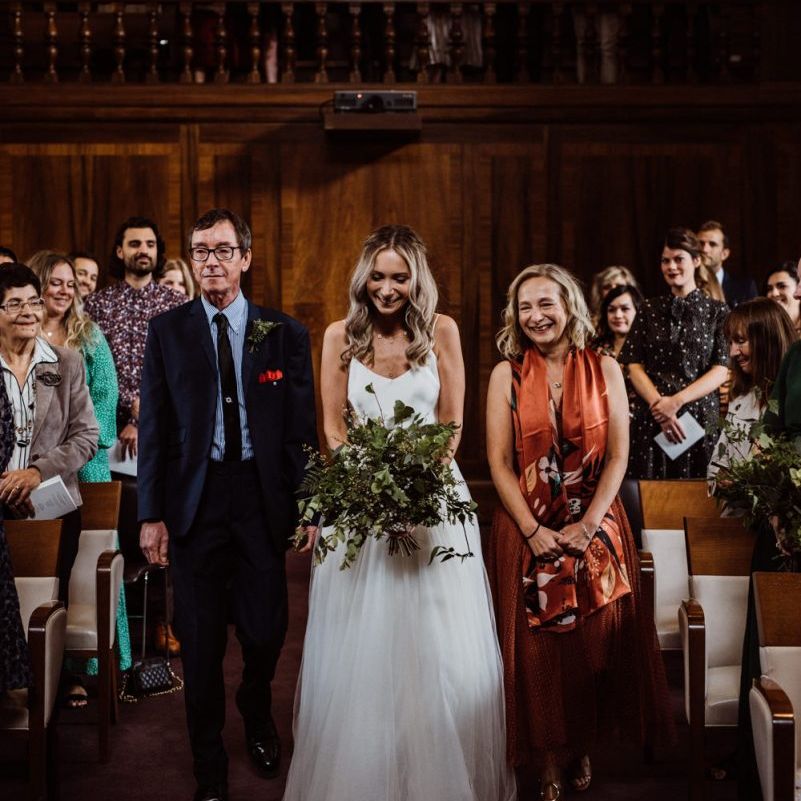 Bride walking down the aisle at Stoke Newington Town Hall wearing two piece gown and foliage bouquet