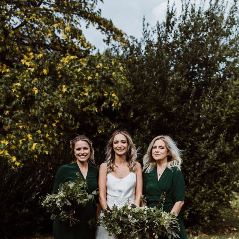 Bride and bridesmaids wearing emerald green dresses and foliage bouquets
