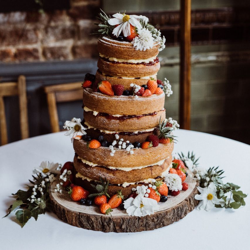 Naked wedding cake with berry and floral decorations on rustic tree stump stand