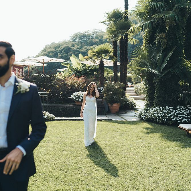 Bride in Grace Loves Lace Wedding Dress Approaching Groo in Navy Suit for First Look