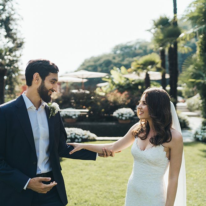 Bride in Grace Loves Lace Wedding Dress Approaching Groom in Navy Suit for First Look