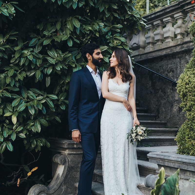 Bride in Grace Loves Lace Mia Wedding Dress and Groom in Taliare Navy Suit Embracing on Steps