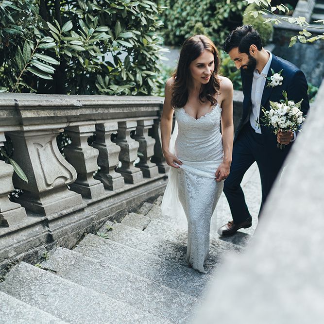 Bride in Grace Loves Lace Mia Wedding Dress and Groom in Taliare Navy Suit Walking up Steps