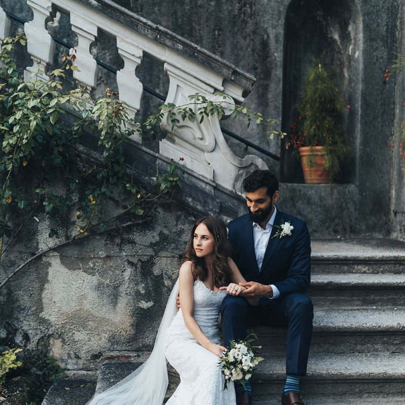 Bride in Grace Loves Lace Mia Wedding Dress and Groom in Taliare Navy Suit Sitting on Steps