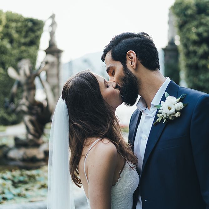 Bride in Grace Loves Lace Mia Wedding Dress and Groom in Taliare Navy Suit  Kissing in Garden