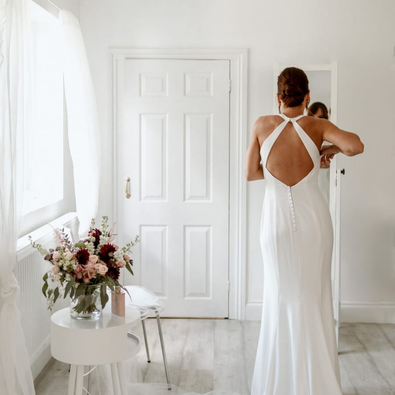 Bride on wedding morning putting on a halter neck dress