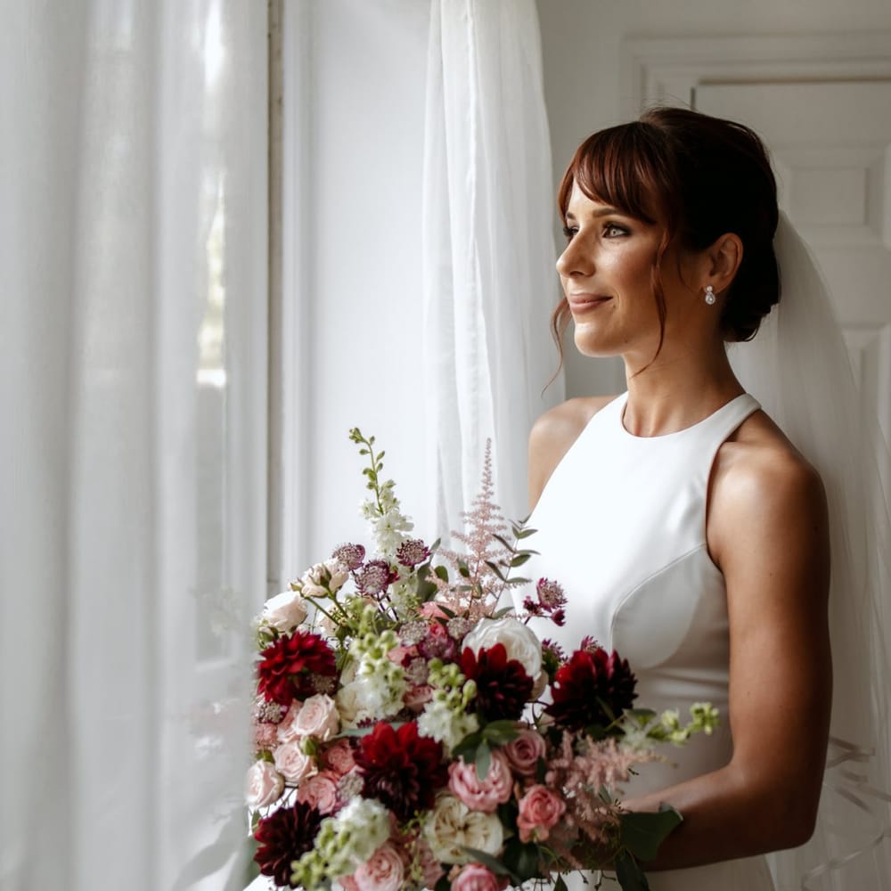 Bride in minimalist wedding dress holding a pink and red bouquet