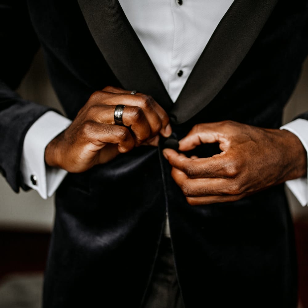 Groom tying up the buttons on his blue velvet jacket