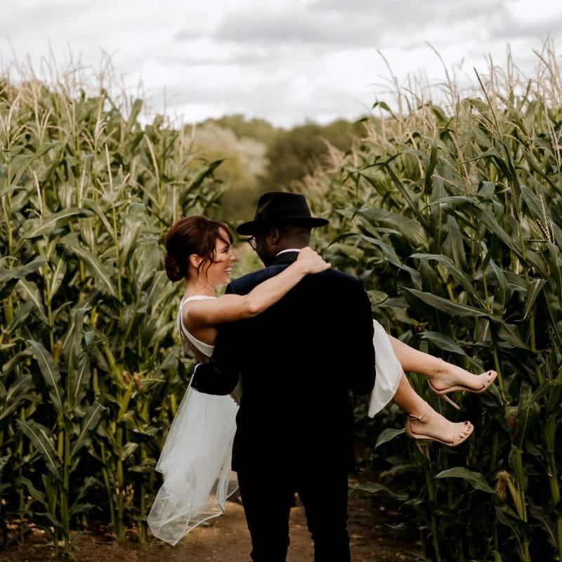 Stylish groom in velvet dinner jacket and Fedora hat picking up his bride