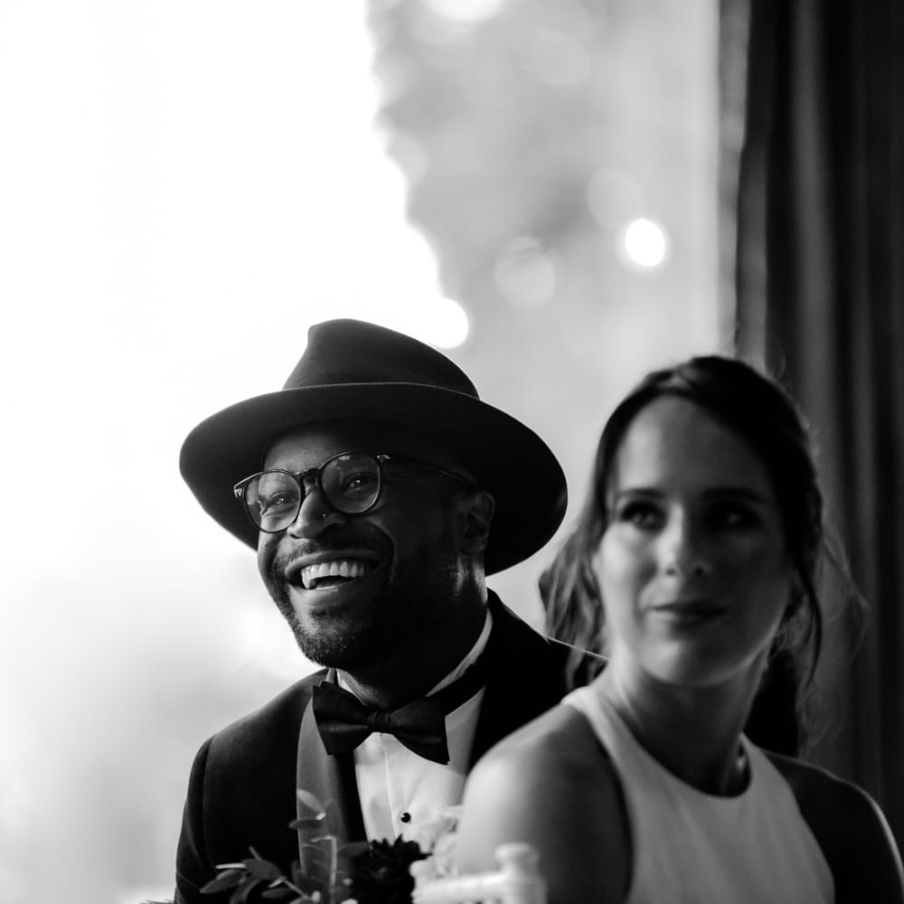 Stylish groom in Fedora hat smiling during the wedding reception speeches