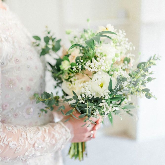 Bride in Needle and Thread Embellished Wedding Dress with Long Sleeves Holding a White and Green Wedding Bouquet
