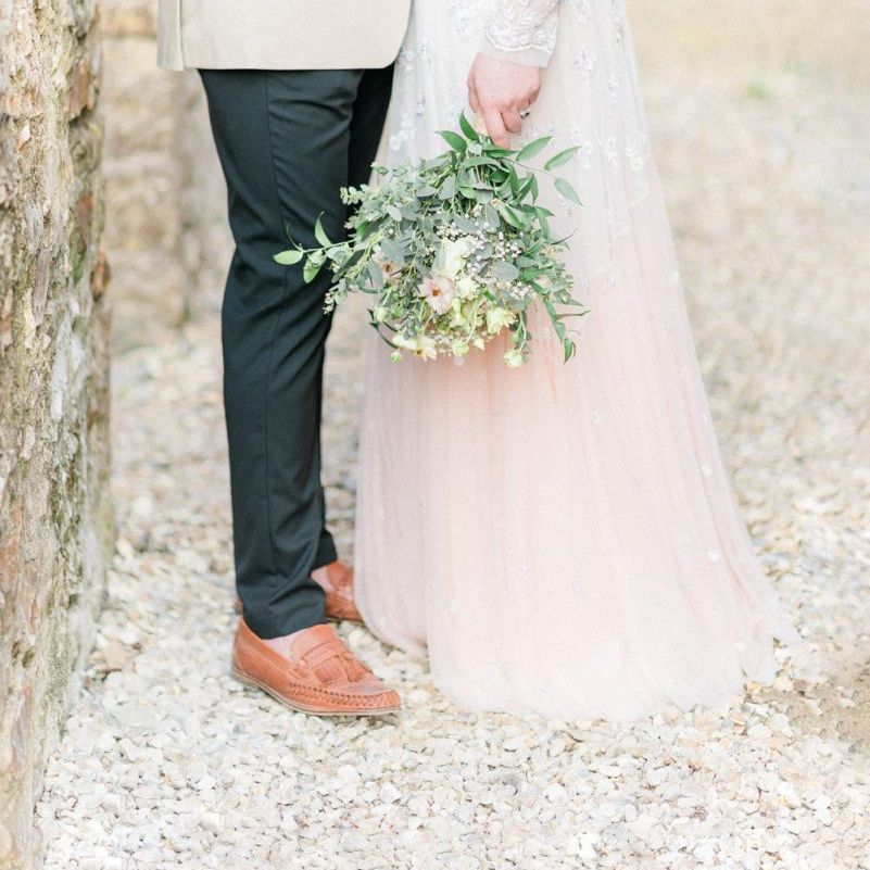 Groom in Black Chino's and Beige Blazer with Tan loafers and Bride in an Ombre Wedding Dress Holding a Bouquet by Her Side
