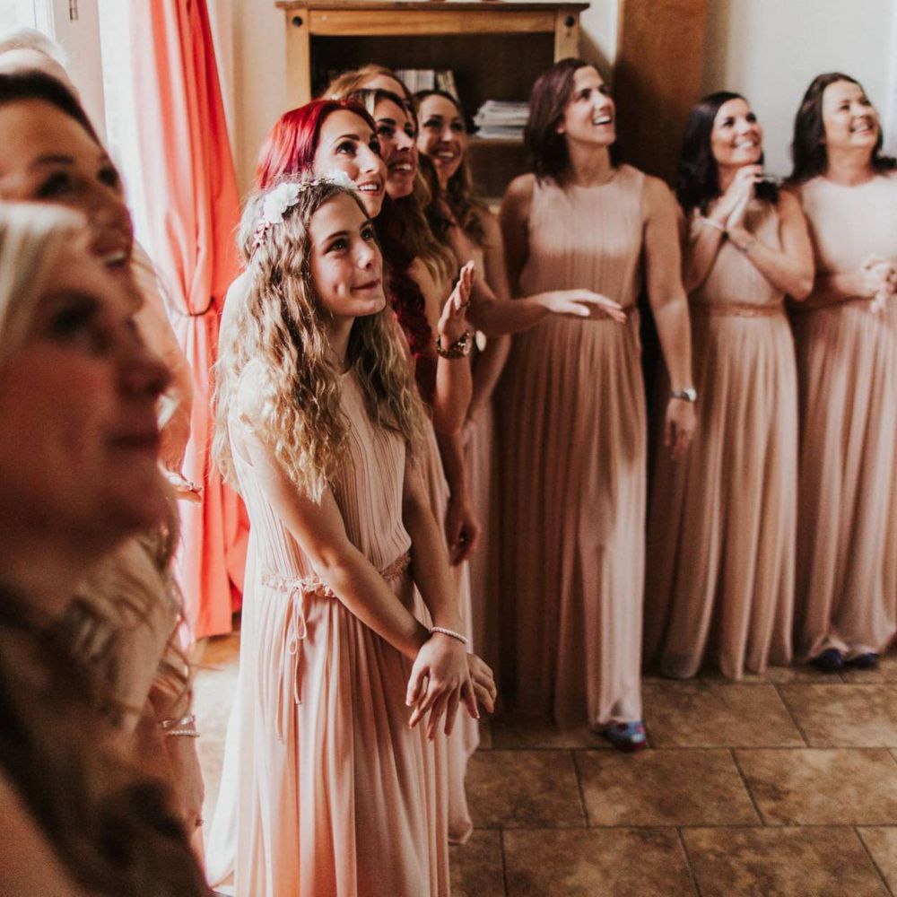 Bridesmaids wearing nude pleated dresses for outdoor summer ceremony with rose floral bouquets