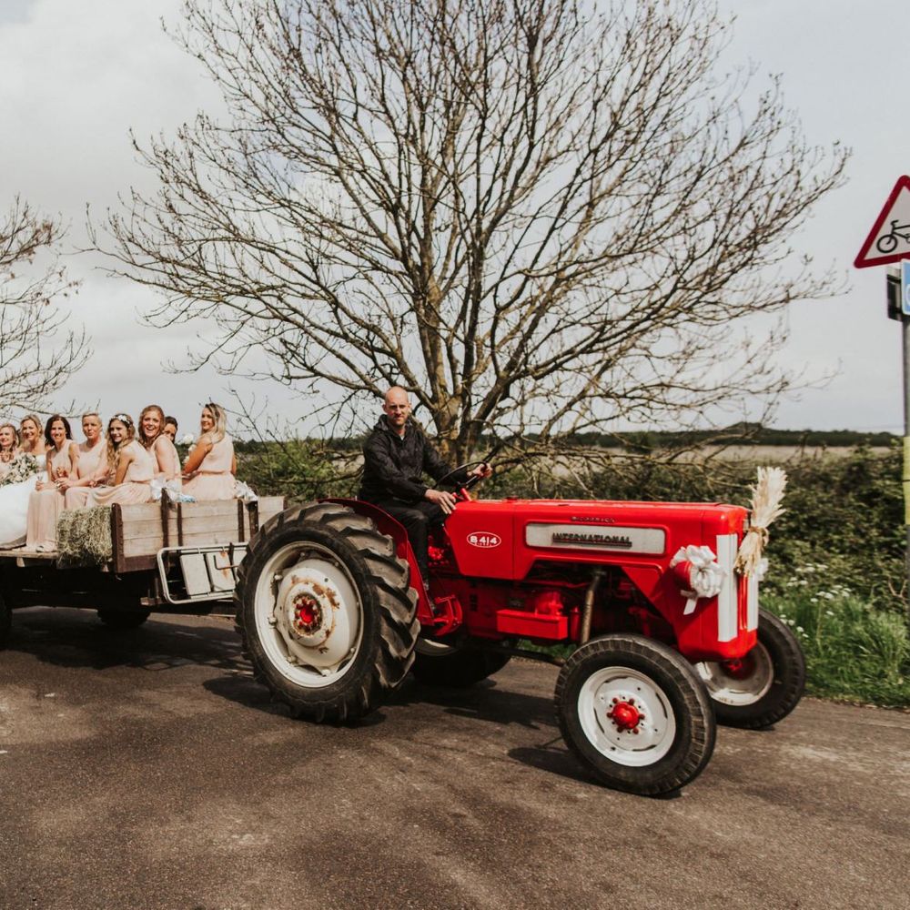 Vintage red tractor transport to the ceremony for the bride and her bridesmaids wearing nude dresses