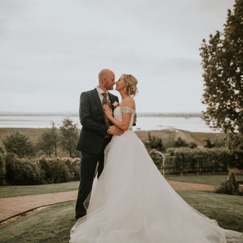 Bride wearing embellished off the shoulder dress with undo hairstyle and groom wearing navy blue suit