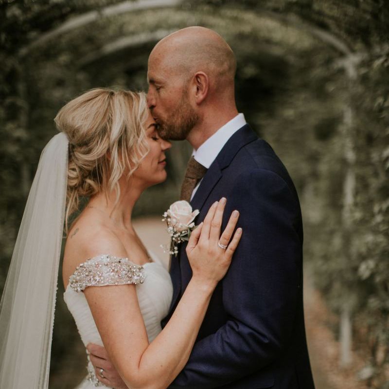 Bride and groom embrace at The Ferry House Inn with embellished off the shoulder dress and navy blue suit