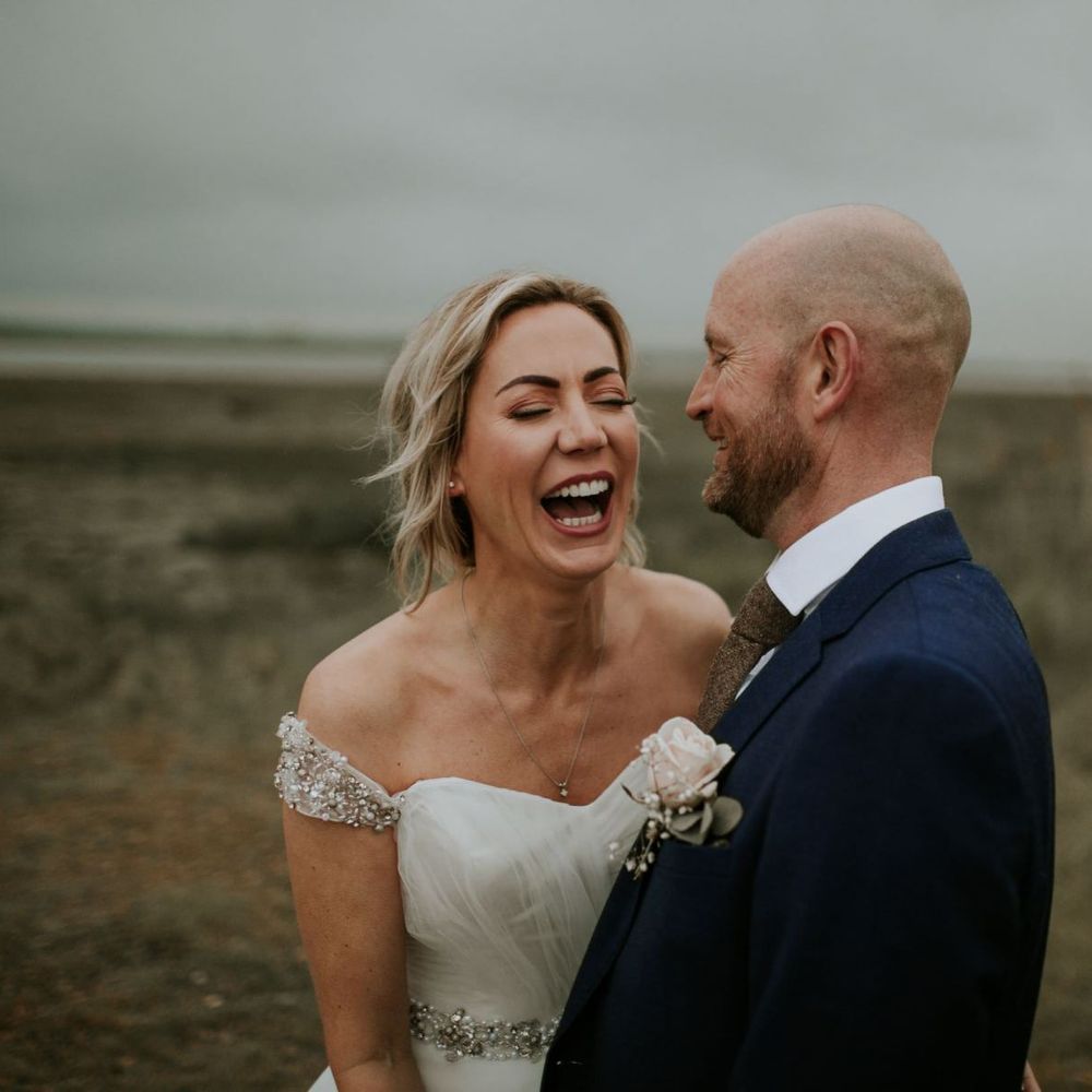 Bride and groom steal a moment at summer wedding wearing embellished of the shoulder dress