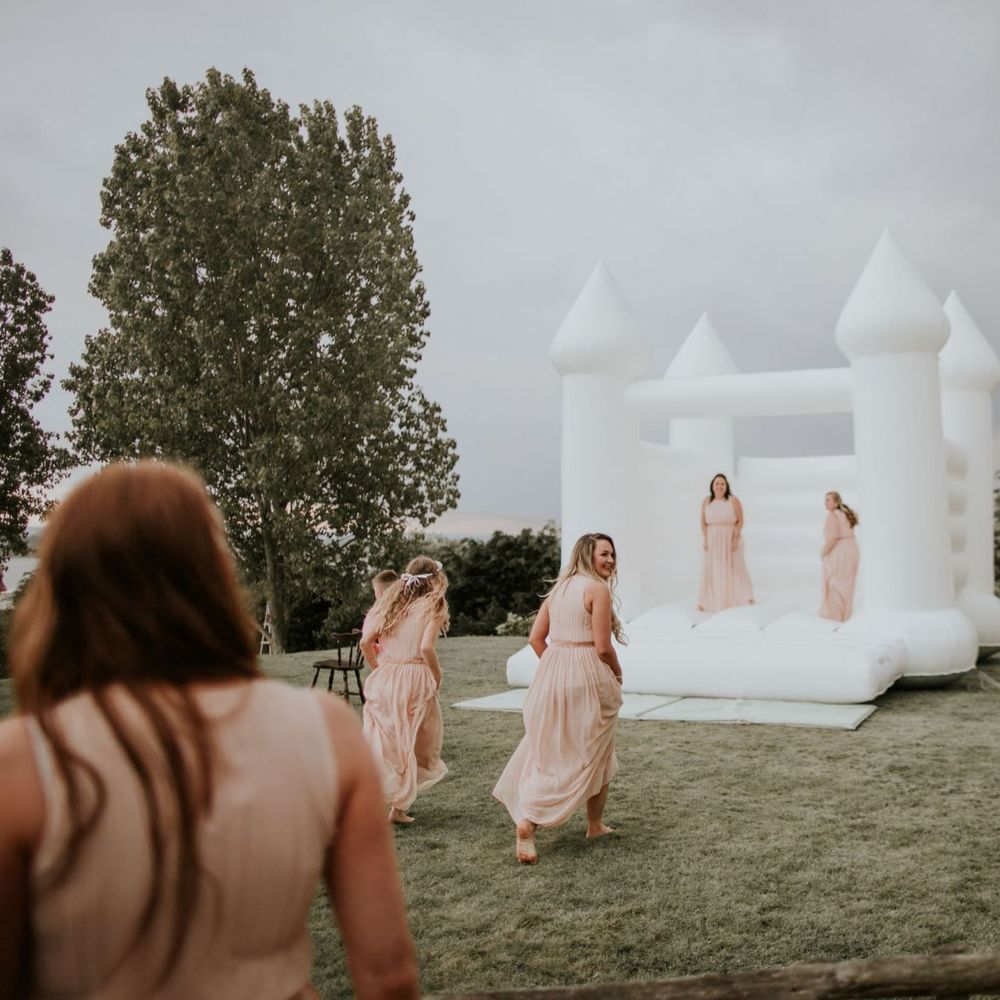 Bride and her bridesmaids wearing nude dresses enjoy white bouncy castle at The Ferry House Inn wedding