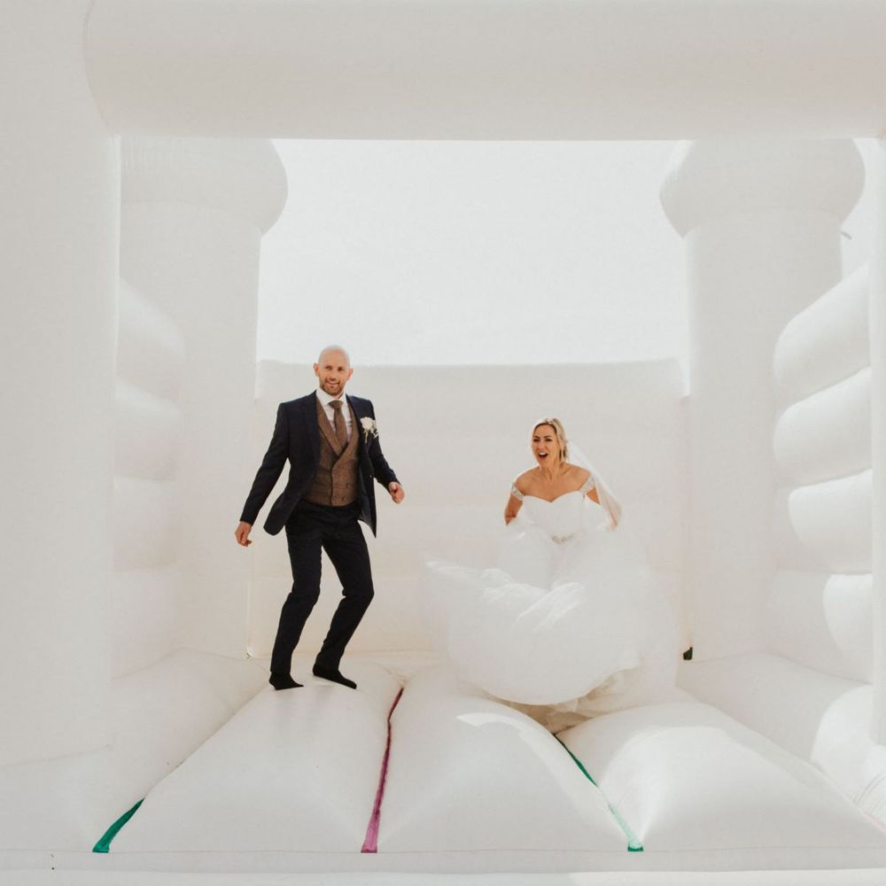Bride and groom at outdoor celebration with white bouncy castle