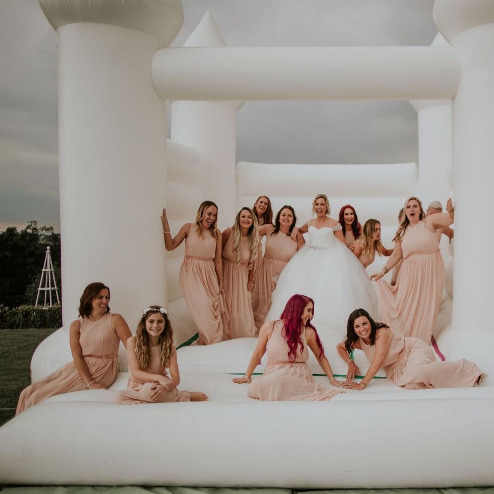 Bride and her bridesmaids wearing nude dresses enjoy white bouncy castle at The Ferry House Inn wedding