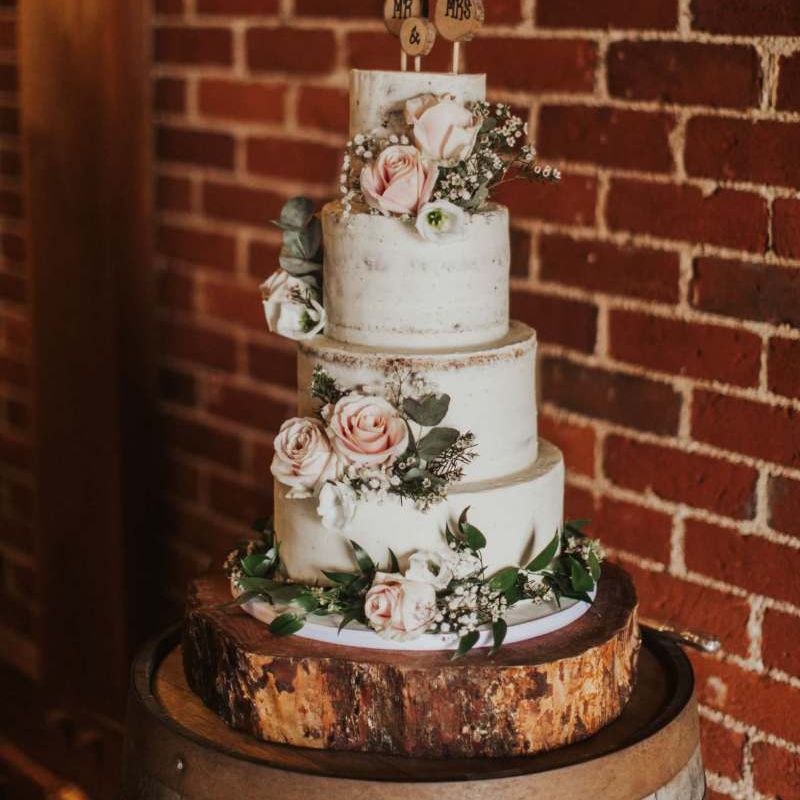 Semi naked cake with pink rose decor on tree stump stand for rustic wedding