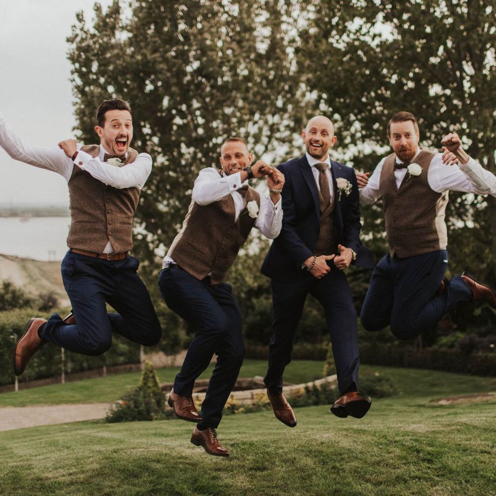 Groom and his groomsmen at outdoor wedding wearing brown waistcoats and navy blue trousers