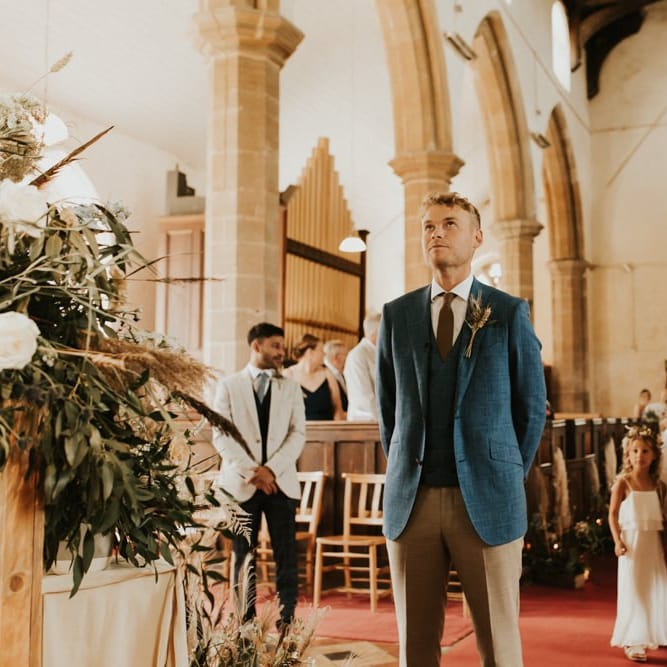 Groom in blue blazer and waistcoat standing at the altar waiting for his bride
