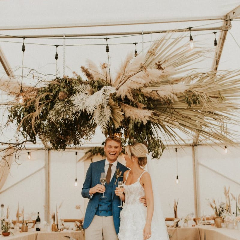Bride in Galia Lahav wedding dress and groom in blue blazer standing in their boho marquee reception for an August 2020 wedding