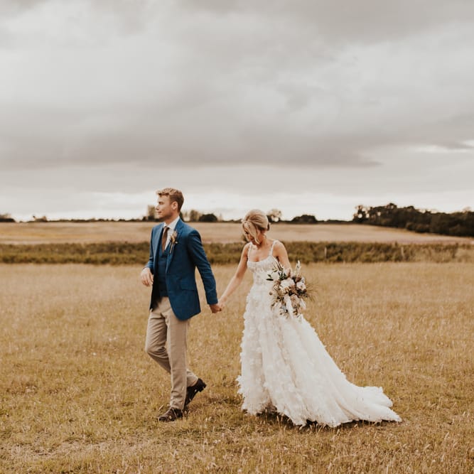 Boho bride and groom walking through the fields at their August 2020 wedding