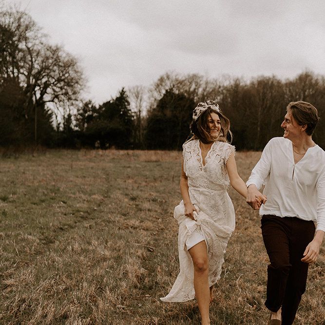 Boho Bride in Lace Wedding Dress and Groom in Casual Trousers and Shirt Running Through The Fields