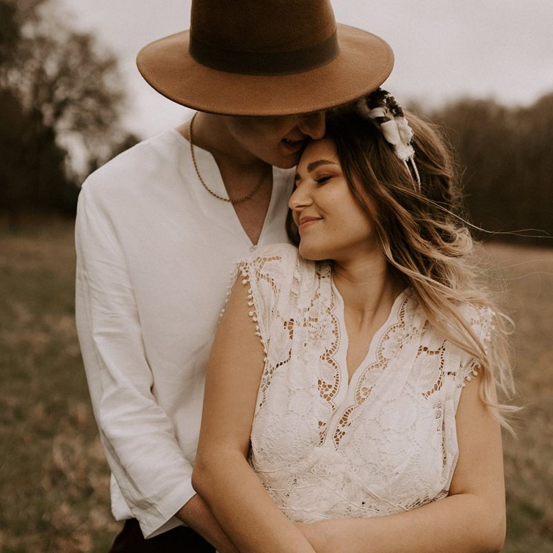 Groom in Fedora Hat Kissing His Boho Bride in a Lace Wedding Dress