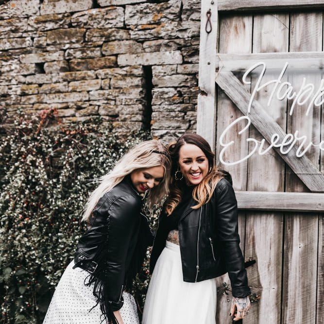 Same sex brides standing next to a neon sign