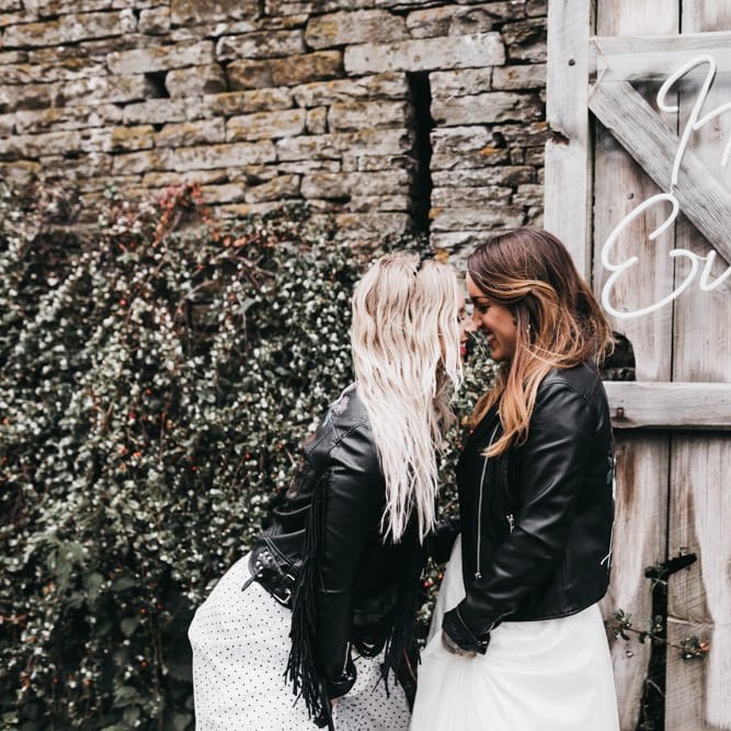 Rock n Roll brides in leather jackets standing next to a neon sign