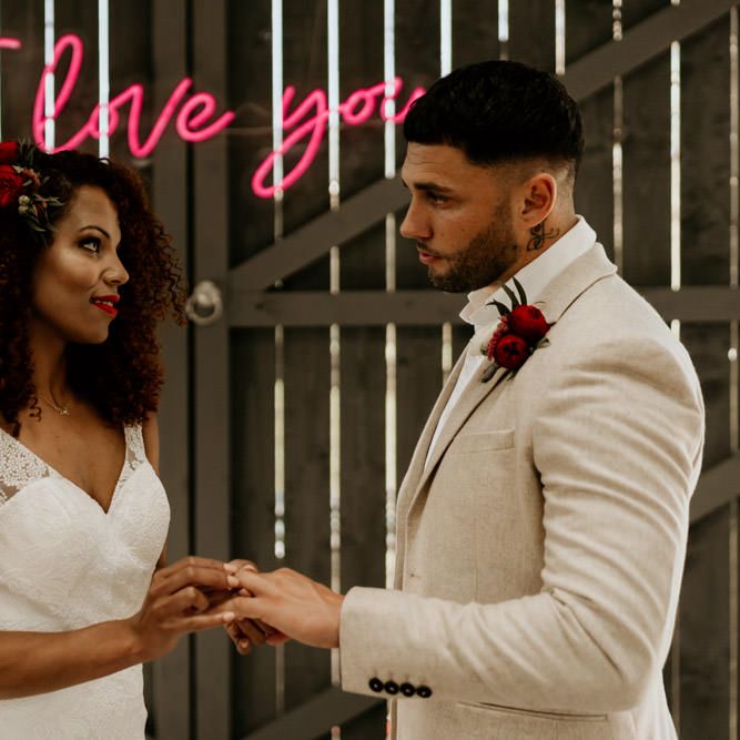 Black Bride with Afro Hair in a Lace Wedding Dress and Groom in Blazer Exchanging Vows Under a Neon Wedding Sign