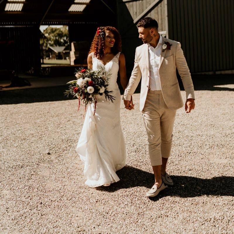 Black Bride with Afro Hair in a Lace Wedding Dress and Groom in Blazer Holding Hands