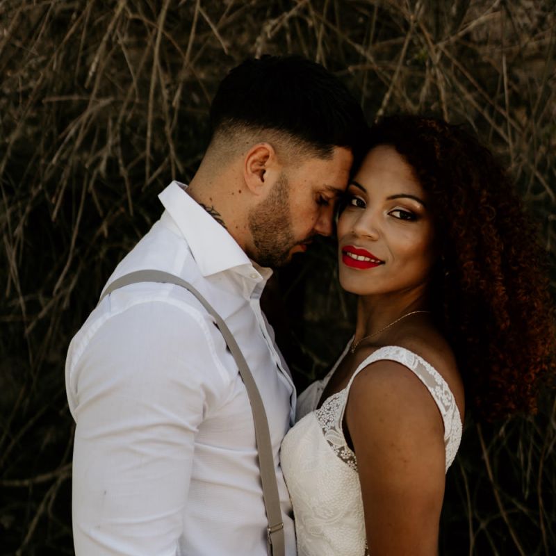 Black Bride with Afro Hair in a Lace Wedding Dress and Groom in White Shirt and Braces Embracing