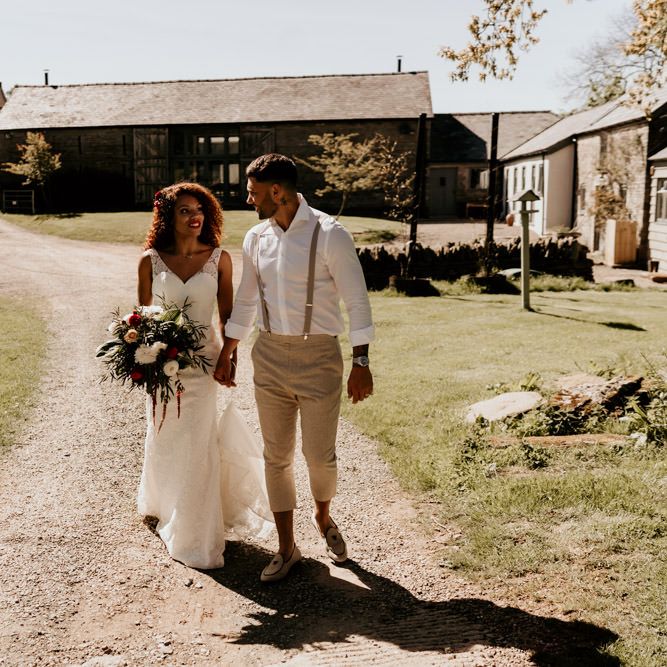 Black Bride with Afro Hair in a Lace Wedding Dress and Groom in White Shirt and Braces Walking Through the Barn