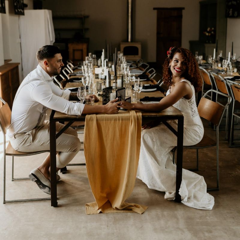 Black Bride in Lace Wedding Dress Holding Hands with Her Groom Across The  Table