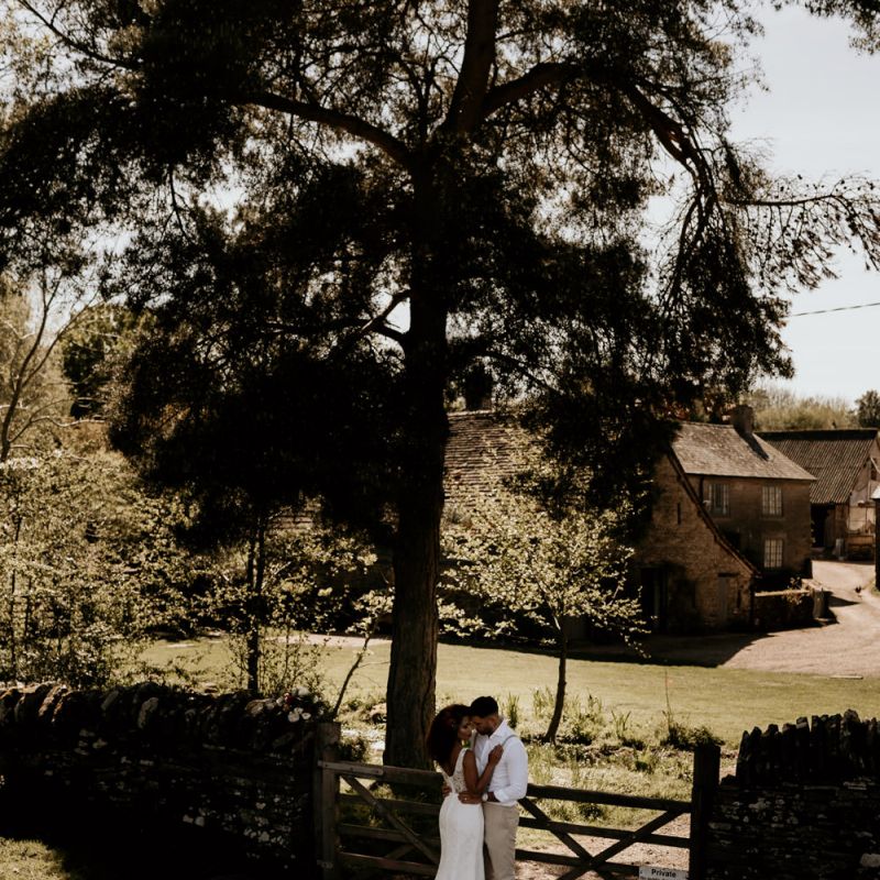 Black Bride in Lace Wedding Dress and Groom in White Shirt and Trousers Embracing in the Field